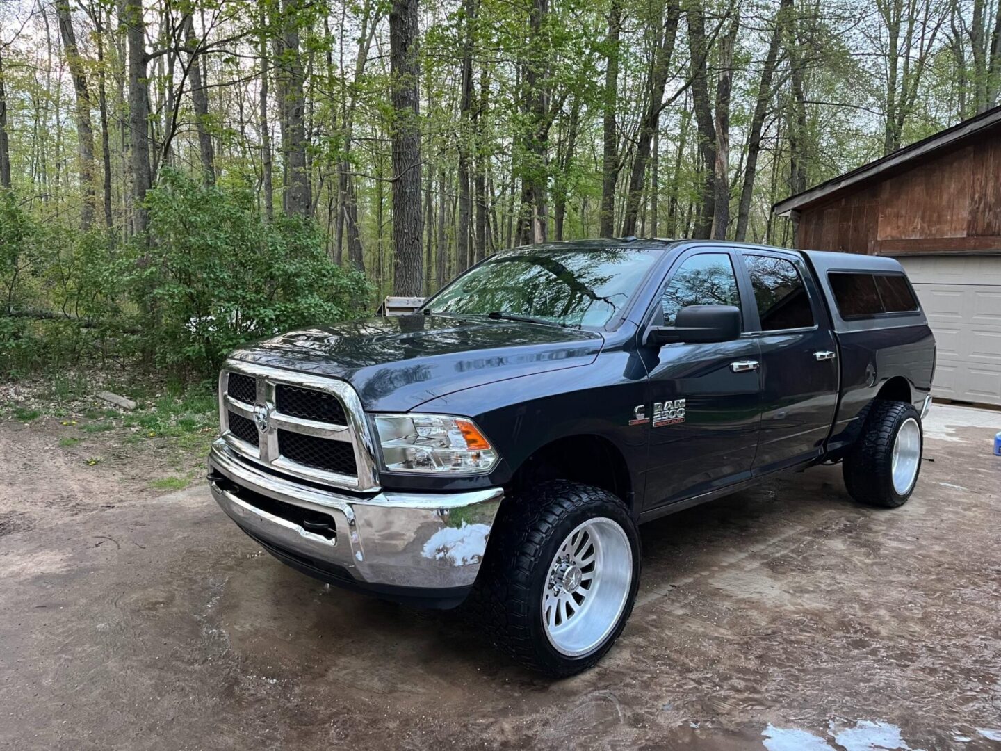 A black truck parked in the dirt near some trees.